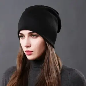 Schwarze Beanie, getragen von einer Frau, frontal vor grauem Hintergrund