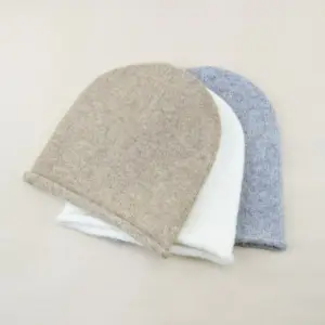 Beige Beanie mit gerolltem Rand, zwei weitere Mützen dahinter, auf beigem Hintergrund
