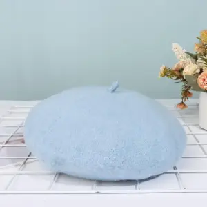 Hellblaues Barett mit kleinem Stiel auf einem Tisch mit Blumen im Hintergrund