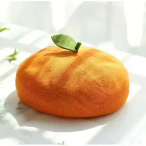 Orangefarbene Baskenmütze in Mandarinenform mit grünem Blatt auf hellem Untergrund