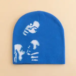01-58 Blaue Strickmütze mit weißem grafischem Motiv, flach auf beigem Hintergrund