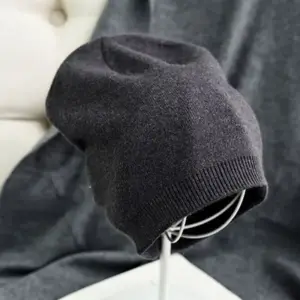Graue Beanie aus feinem Strick auf einem Mützenständer vor grauer Decke